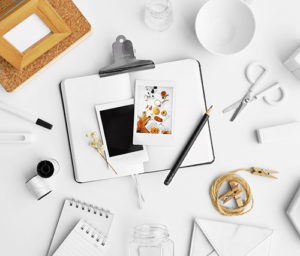 White themed photo of Toms River website designer desk covered with scissors, pencils, thread, photos, and a clipboard