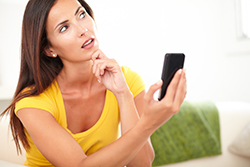 Woman in yellow top with questioning look on face while staring at website on mobile phone